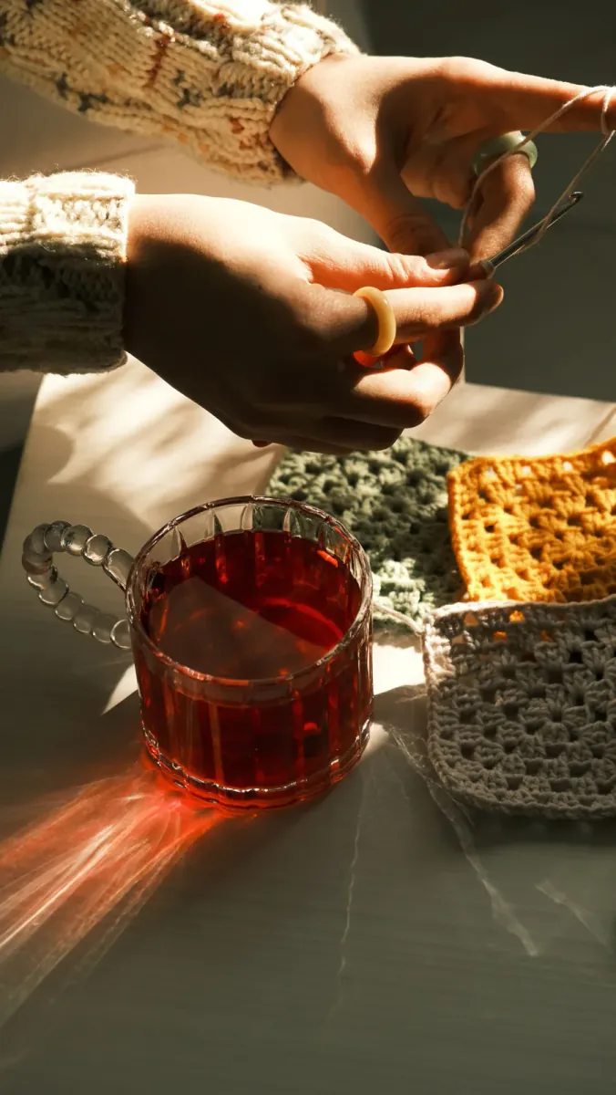 Hands crocheting granny squares in sage and sunflower cotton yarn in warm afternoon light